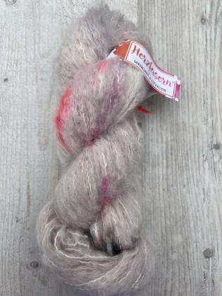 „Flauschiger Strang aus Baby-Suri-Alpaka und Seide in nebligen Grau- und Beigetönen mit Pink- und Grünakzenten; fotografiert auf hellem Holzuntergrund mit Herzfasern-Etikett.“